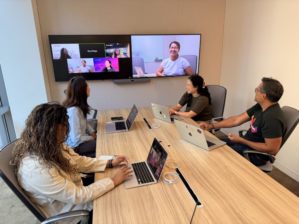 Team meeting in a conference room with a video call on screen.