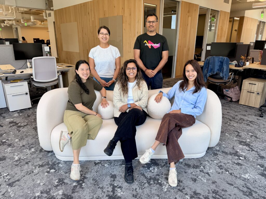 Five Airwallex employees posing together on and behind a white sofa in a modern office.